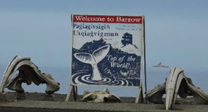 Bowhead whale skulls alongside the “Welcome to Barrow” sign with the Oden sitting offshore in the background at right.