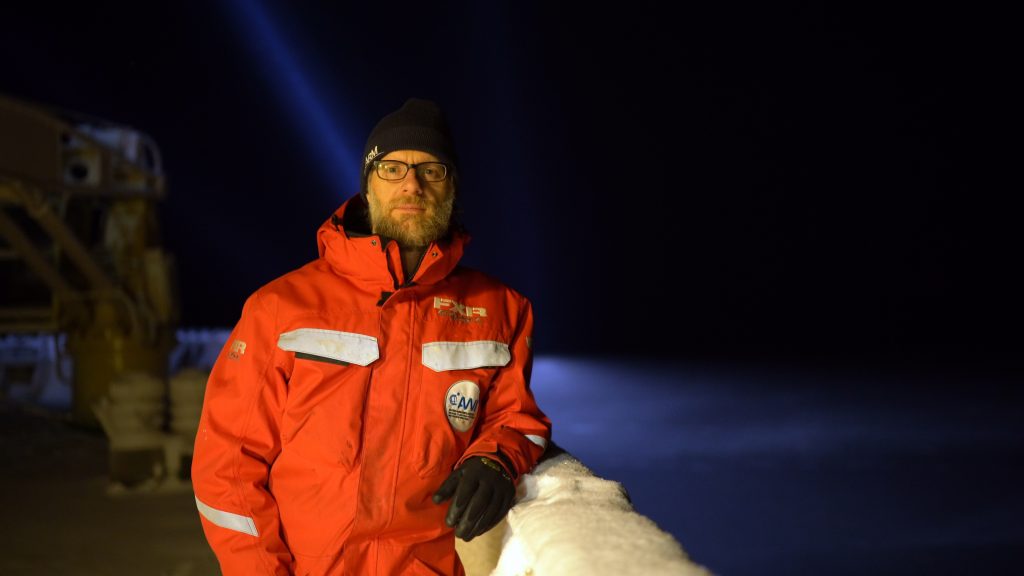 Man stands in orange snow suit on ship at night